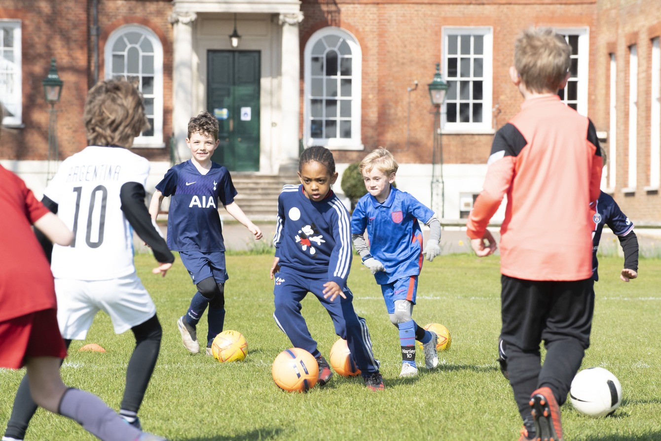 A young child's feet skillfully dribbling a football around a series of orange cones during a practice session.